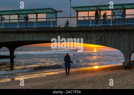Bournemouth, Dorset UK. 1. Dezember 2019. UK Wetter: atemberaubende Sonnenuntergang am Strand von Bournemouth am Ende einer bitter kalt trockenen sonnigen Wintertag. Person zu Fuß entlang der Küste nach Bournemouth Pier bei Sonnenuntergang, während andere am Pier entfernt. Credit: Carolyn Jenkins/Alamy leben Nachrichten Stockfoto