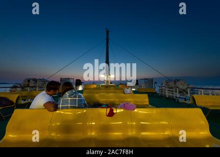 Die Passagiere sitzen auf Reihen von gelben Kunststoff sitze auf dem oberen Deck der Fähre im Zadar Archipels nach Sonnenuntergang in der Dämmerung, Kroatien Stockfoto