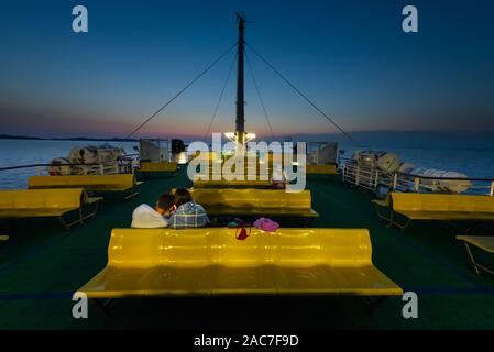 Die Passagiere sitzen auf Reihen von gelben Kunststoff sitze auf dem oberen Deck der Fähre im Zadar Archipels nach Sonnenuntergang in der Dämmerung, Kroatien Stockfoto