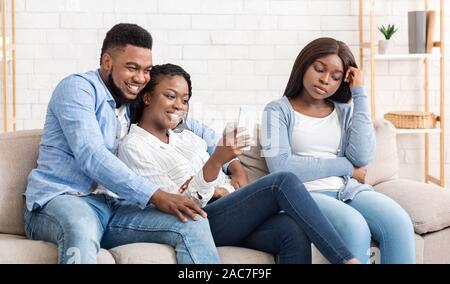 Eifersüchtig schwarze Mädchen sitzt in der Nähe von romantischen Paar auf , traurig Stockfoto