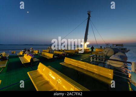 Die Passagiere sitzen auf Reihen von gelben Kunststoff sitze auf dem oberen Deck der Fähre im Zadar Archipels nach Sonnenuntergang in der Dämmerung, Kroatien Stockfoto