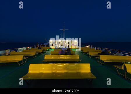 Die Passagiere sitzen auf Reihen von gelben Kunststoff sitze auf dem oberen Deck der Fähre im Zadar Archipels nach Sonnenuntergang in der Dämmerung, Kroatien Stockfoto