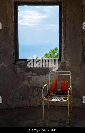 Kaputter Stuhl vor dem Fenster auf, das von den Ruinen einer Festung aus dem 19. Jahrhundert an der Hum Berg in der Nähe der Stadt Velu Luka, Insel Korcula, Kroatien Stockfoto
