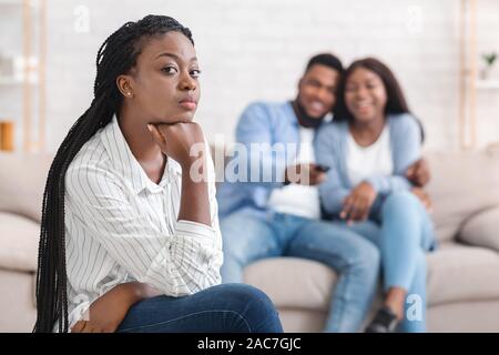 Neid Mädchen sitzt allein, während Ihr dating Freunde Umarmen auf der Couch Stockfoto