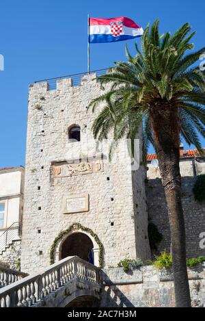 Historische Gate Tower von Korčula Veliki Revelin mit kroatischen Flagge und einer Palme, Insel Korcula, Dalmatien, Kroatien Stockfoto