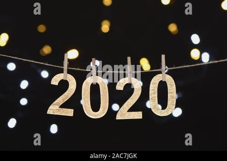 Neues Jahr 2020 im goldenen Holz Buchstaben hängen an einem Seil mit Unkonzentrierten leuchtet auf schwarzem Hintergrund, Zusammensetzung als Postkarte Stockfoto