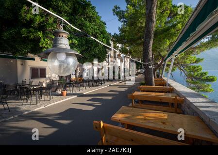 Lampe vor leeren Tischen und Stühlen auf der Terrasse des Restaurants auf der Stadtmauer der Altstadt von Korcula in der Morgensonne, Kroatien Stockfoto