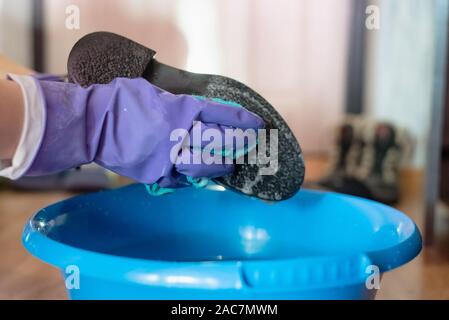 Frau in der Handschuhe Reinigung ihre Stiefel durch einen Lappen in Seifenwasser. Stockfoto