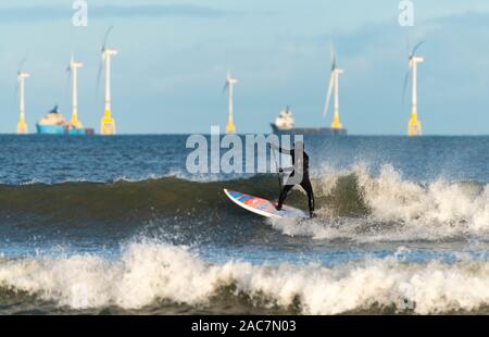 Aberdeen, Schottland, Großbritannien. Dezember 2019. Surfer nutzten den hellen Sonnenschein und die günstigen Winde, die gute Wellen am Strand von Aberdeen schufen. In der Ferne befinden sich Offshore-Windenergieanlagen des Windparks European Offshore Wind Deployment Center. Iain Masterton/Alamy Live News. Stockfoto