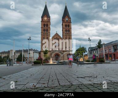 Abend Blick der Twin überragte Unsere Liebe Frau von Ungarn Römisch-katholische Kirche mit Brunnen im Vordergrund. Szeged, Ungarn. Stockfoto