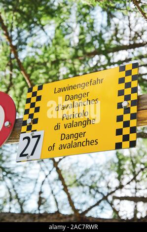 Gelbe touristische Schild warnt vor Lawinen in vier verschiedenen Sprachen. Warnung in Deutsch, Französisch, Italienisch und Englisch. Informationen für Touristen in den Schweizer Alpen. Stockfoto