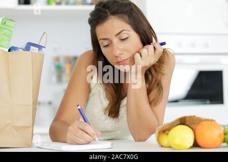 Frau in der Küche mit Shopping schriftlich im Notebook Stockfoto