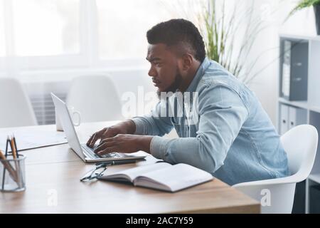 Junge afrikanische Arbeiter mit Laptop im Büro Stockfoto