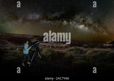 Junger Mann beobachtet Sternenhimmel durch ein Teleskop. In den Bergen, umgeben von Pinienwald im Hintergrund Nacht Landschaft mit bunten Milchstraße Stockfoto