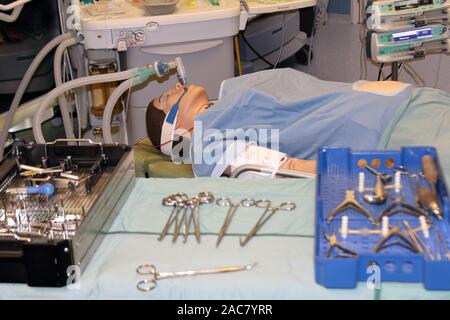 Eine simulierte Operation, bei der ein Patient (Manakin) und ein Anästhesiegerät im Hintergrund und chirurgische Instrumente im Vordergrund angezeigt werden Stockfoto