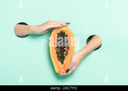 Weibliche Hände halten frischer Papaya durch ein Loch auf Neon mint Hintergrund. Stockfoto