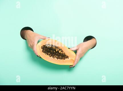 Weibliche Hände halten frischer Papaya durch ein Loch auf Neon mint Hintergrund. Stockfoto