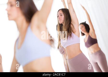 Gruppe von jungen sportlich attraktive Frauen im Yoga Studio, Yoga Unterricht mit Kursleiter, stehend, Stretching und Entspannung nach dem Training Stockfoto
