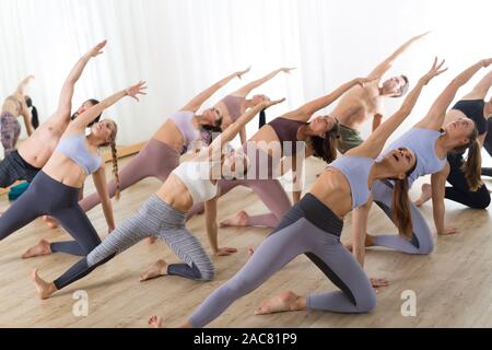 Gruppe von jungen sportlich attraktive Leute im Yoga Studio, Yoga Unterricht mit Kursleiter, Stretching auf Fußboden im Trikonosana, Dreieck yoga Pose Stockfoto