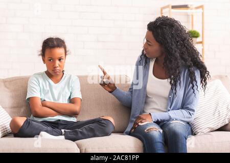 Grumpy schwarz Mutter ihre freche kleine Tochter auf Sofa Schelte zu Hause Stockfoto