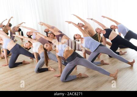 Gruppe von jungen sportlich attraktive Leute im Yoga Studio, Yoga Unterricht mit Kursleiter, Stretching auf Fußboden im Trikonosana, Dreieck yoga Pose Stockfoto