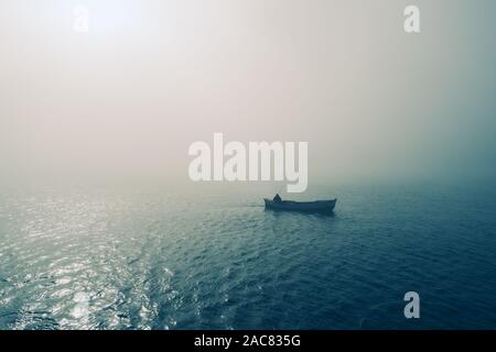 Fischerboot und Fischer im Meer, nebeliger Morgen über das Wasser. Stockfoto