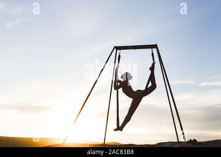 Schlanke Frau üben fliegen Tanz akrobatischen Yoga Posen in der Hängematte im Freien bei Sonnenuntergang. Sport und Wohlbefinden Konzept. Gesunde Lebensweise. Stockfoto