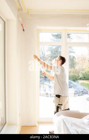 Volle Länge Schoß des jungen Mannes Malerei die Wand in der Wohnung. Stockfoto