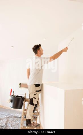 Schuß von professionellen Auftragnehmer stehen auf Leiter und Malerei Wand während der Renovierung der Wohnung.