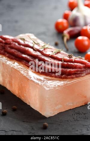 Salz block Kochen. Lean Black Angus Fleisch mariniert auf Himalaya Pink salt Block und Tomaten, Paprika und Knoblauch Seitenansicht Kopie Raum Stockfoto
