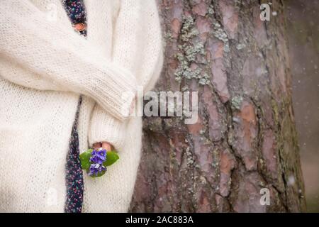 Junge Frau in Weiß Strickjacke in der Nähe von einem alten Baum und halten schöne Schneeglöckchen in den Händen. Erste Frühling Blumen in einem Wald. Anfang Stockfoto