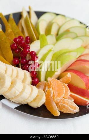 Eine Platte der Jahreszeit frisches Obst und Beeren. Obstsalat. Diät, gesunde Frucht Salat auf die schwarze Platte, gesundes Frühstück, Gewichtsreduktion Konzept. closeup Stockfoto