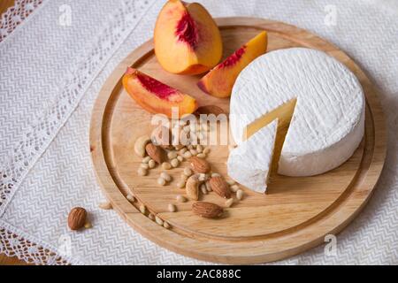 Weiß köstliche hausgemachte camambert Käse auf einem Holzteller serviert mit Mandeln, Cashew, Pinienkernen und Pfirsich. Dessert für ein Abendessen mit der Familie. Stockfoto