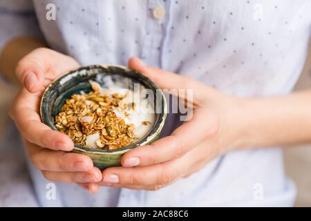 Junge Frau mit Müsli Schüssel. Frühstück Müsli mit Nüssen, Kürbiskerne, Hafer und Joghurt in der Schüssel. Hände, die hausgemachtes Müsli. Gesunden Snack. Stockfoto