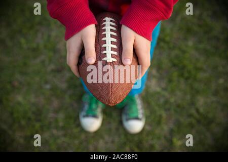 Ansicht von oben auf die Hände von Little kid Boy holding Fußball im Stadion an einem sonnigen Tag. Kind bereit, einen Football zu werfen. Sport Konzept. Sport f Stockfoto
