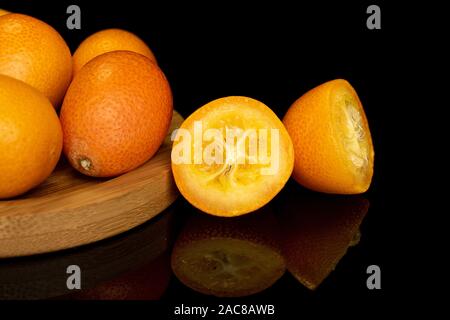 Gruppe von vier ganze zwei Hälften von leckeren orange Kumquat auf runden Bambus Untersetzer auf schwarzem Glas isoliert Stockfoto