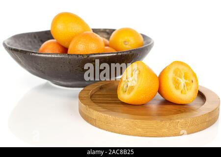 Gruppe von vier ganze zwei Hälften von leckeren orange Kumquat in glasierte Schüssel auf runden Bambus Untersetzer auf weißem Hintergrund Stockfoto