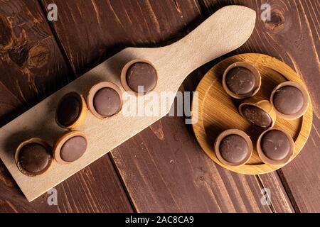 Menge ganz süßen braunen Toffee auf runden Bambus Untersetzer auf Holz Schneidebrett flatlay auf braunem Holz Stockfoto