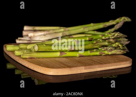 Viele von ganzen frischen gesunden grünen Spargel auf Bambus Schneidbrett auf schwarzem Glas isoliert Stockfoto