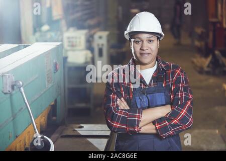 Taille bis Porträt des modernen Arbeiterin tragen, hardhat und Overalls Stehen mit verschränkten Armen, während in Industrieanlagen Posing, kopieren Raum Stockfoto