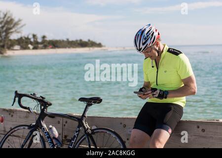 Einen Radfahrer nimmt einen Bruch von seinem morgendlichen Fahrt seine Telefonnummer in Florida zu prüfen. Stockfoto