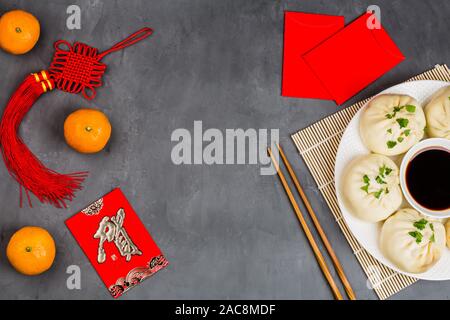 Das chinesische Neujahr Dekoration mit Knödel, Mandarinen, Sojasauce, Stäbchen, roten Briefumschläge auf grauem Beton Hintergrund. Happy Chinese New Year 2020 Stockfoto