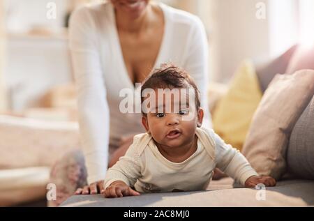 Portrait von niedlichen Afrikaner - Baby suchen Bei camera Beim liegen auf der Couch mit junge Mutter tun, Massage, Kopie Raum Stockfoto