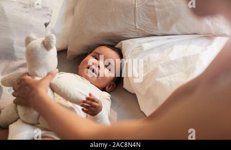 Hohen winkel Portrait von niedlichen Mixed-race Baby an der Mutter beim Spielen mit Bär Spielzeug, Platz kopieren Stockfoto