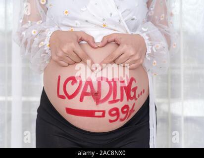 Schwangere Frau Hände halten in Herzform mit gemalten Bürste Wort-Laden 99% auf ihrem Bauch Stockfoto
