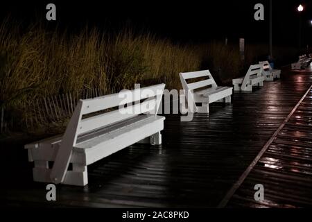 Leere weiße Bänke auf Rehoboth Beach Promenade in der Nebensaison, wie man sie in einer nassen Nacht sieht. Stockfoto