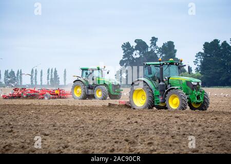 Sheffield, Canterbury, Neuseeland, 30. November 2019: John Deere Traktoren bei der Arbeit in einem Feld, den Boden zu kultivieren bereit für Kartoffeln gepflanzt zu werden Stockfoto