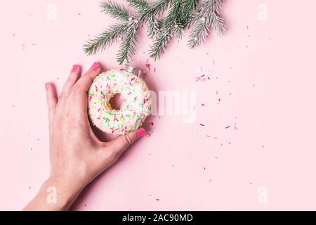 Weibliche Hand hängt Christmas Ball von donut auf rosa Hintergrund gemacht. Weihnachten kreative Konzept. Stockfoto