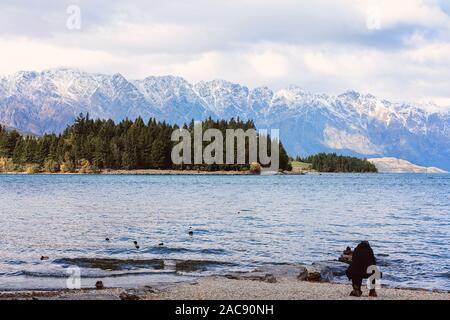 Silhouette eines Fotografen hocken unten ein Foto von einem Vogel am Ufer des Lake Wakatipu in Neuseeland zu nehmen Stockfoto