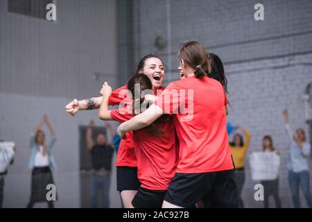 Ekstatisch Mädchen im Sport einheitliche Umarmung nach dem erfolgreichen Ziel während des Spiels auf Fußball-Feld Stockfoto